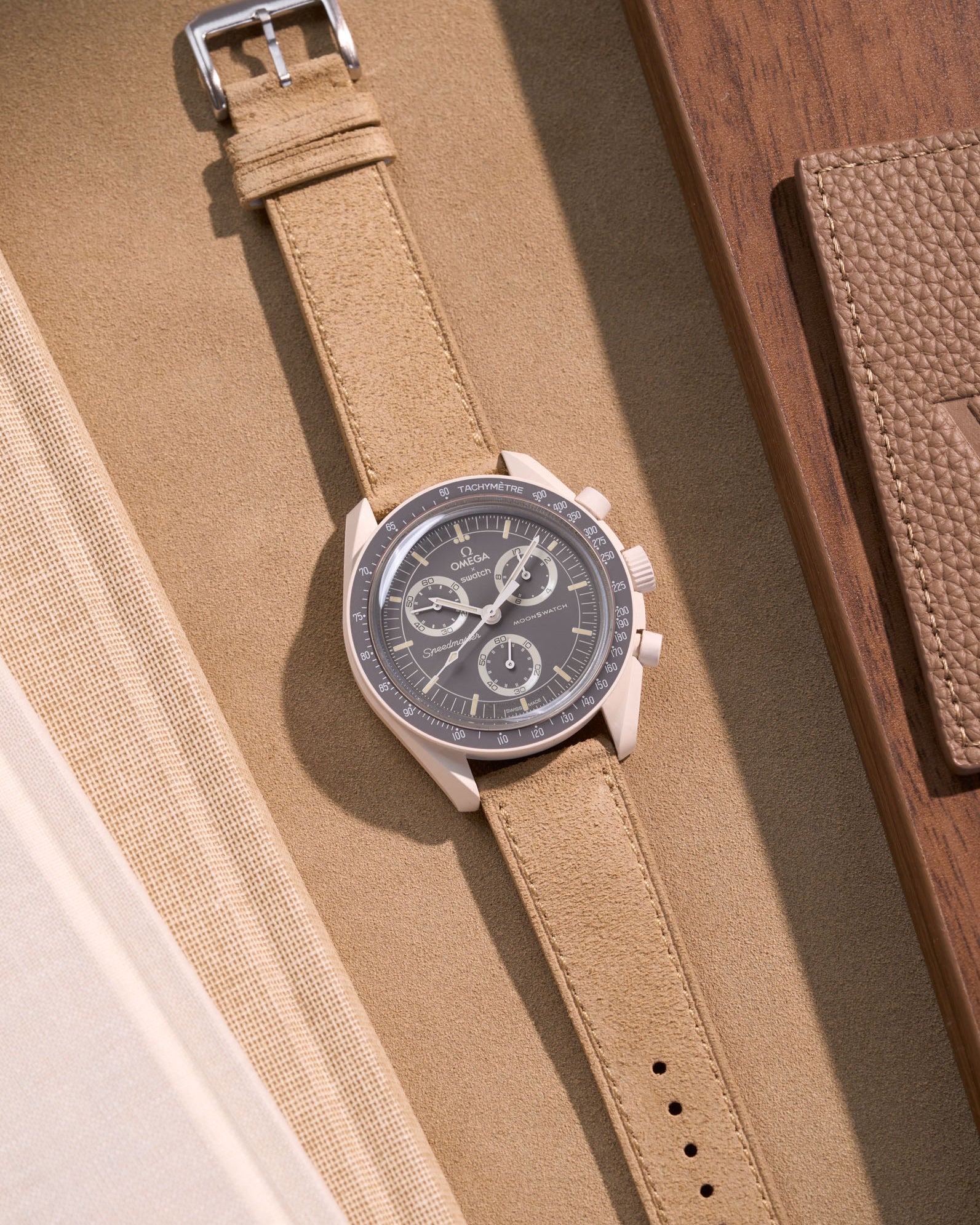 Flat lay of Omega X Swatch Mission on Earth – Desert with Beige suede leather strap, styled with brown and neutral accessories