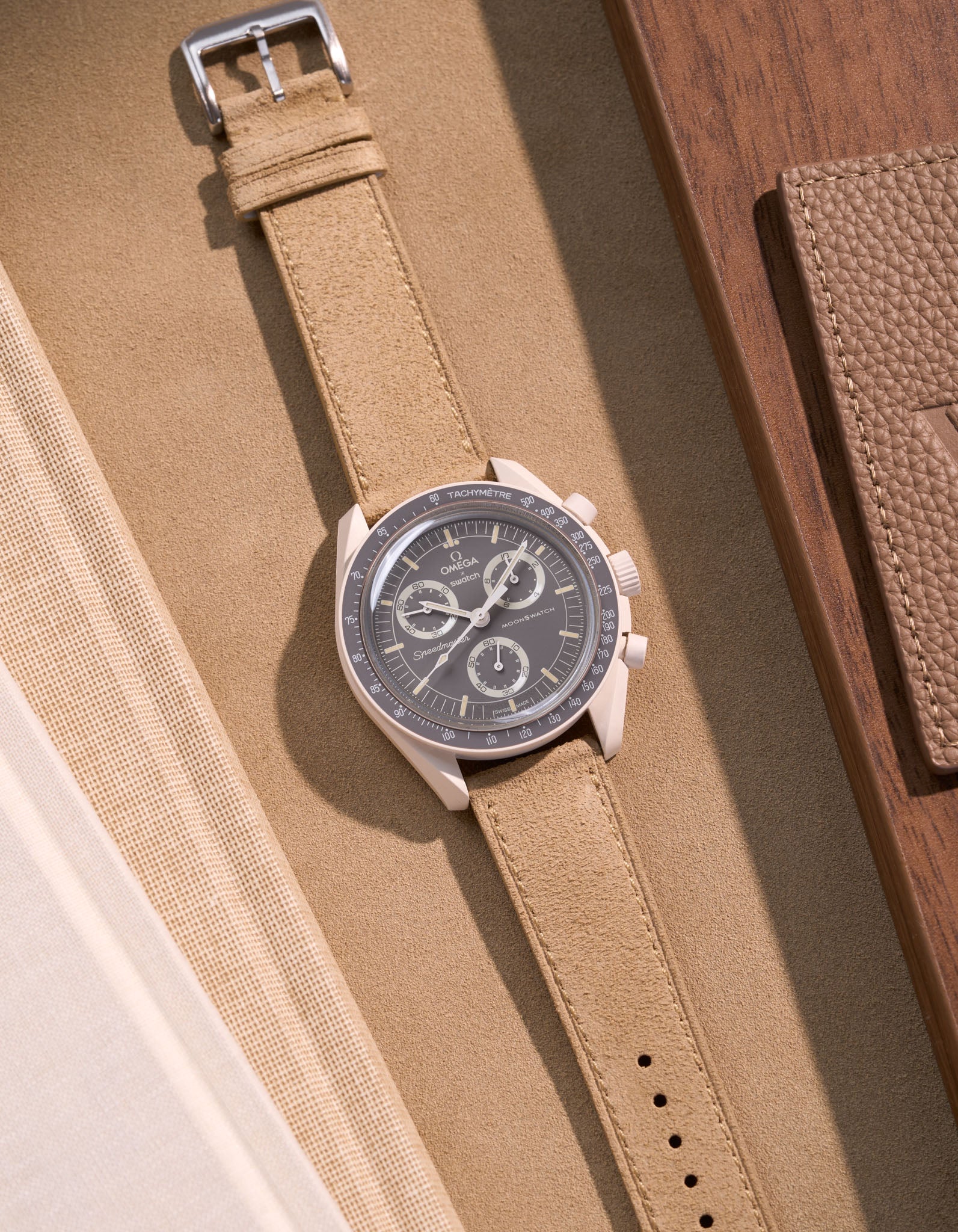 Flat lay of Omega X Swatch Mission on Earth – Desert with Beige suede leather strap, styled with brown and neutral accessories