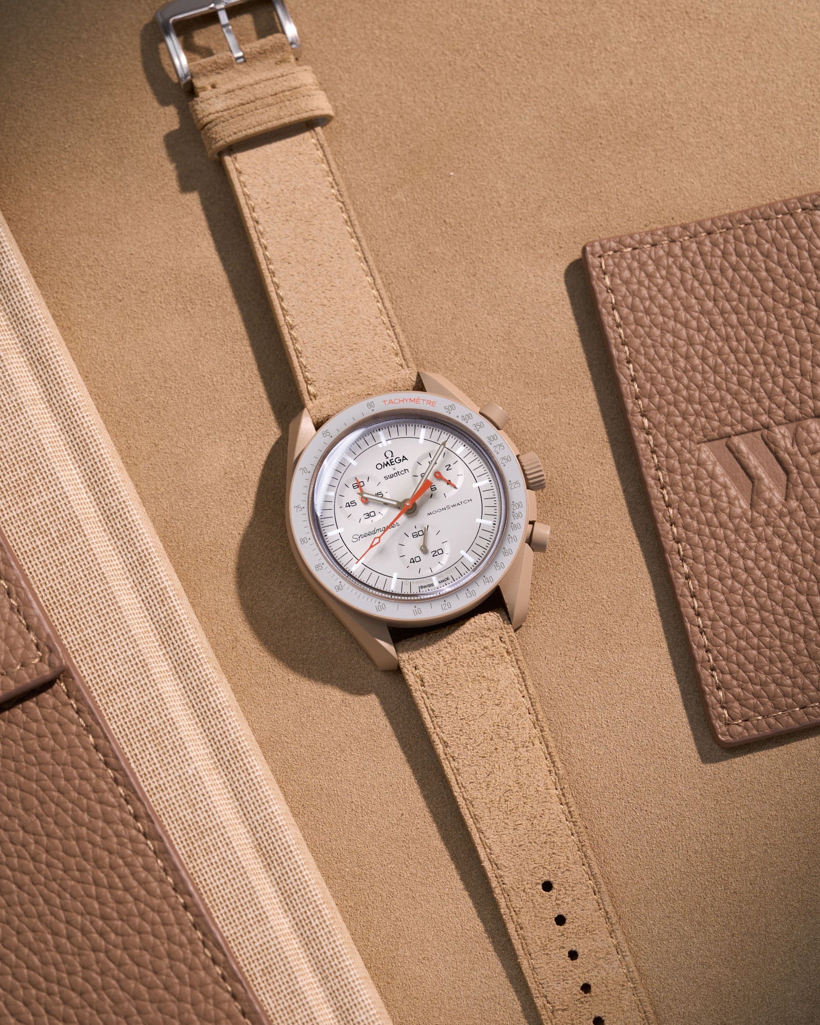 Flat lay of Omega X Swatch Mission to Jupiter with Beige suede leather strap, styled with neutral and warm brown accessories