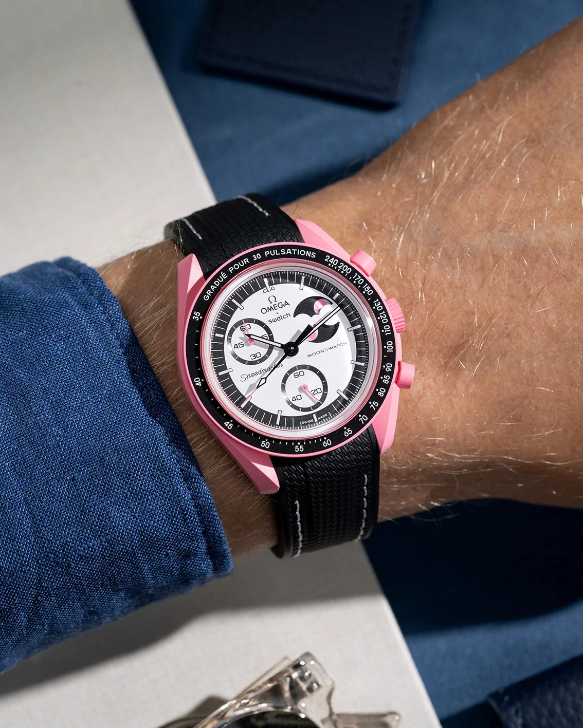 Wrist shot showing black rubber strap with white stitching for Omega X Swatch MoonSwatch Mission to the Pink Moonphase