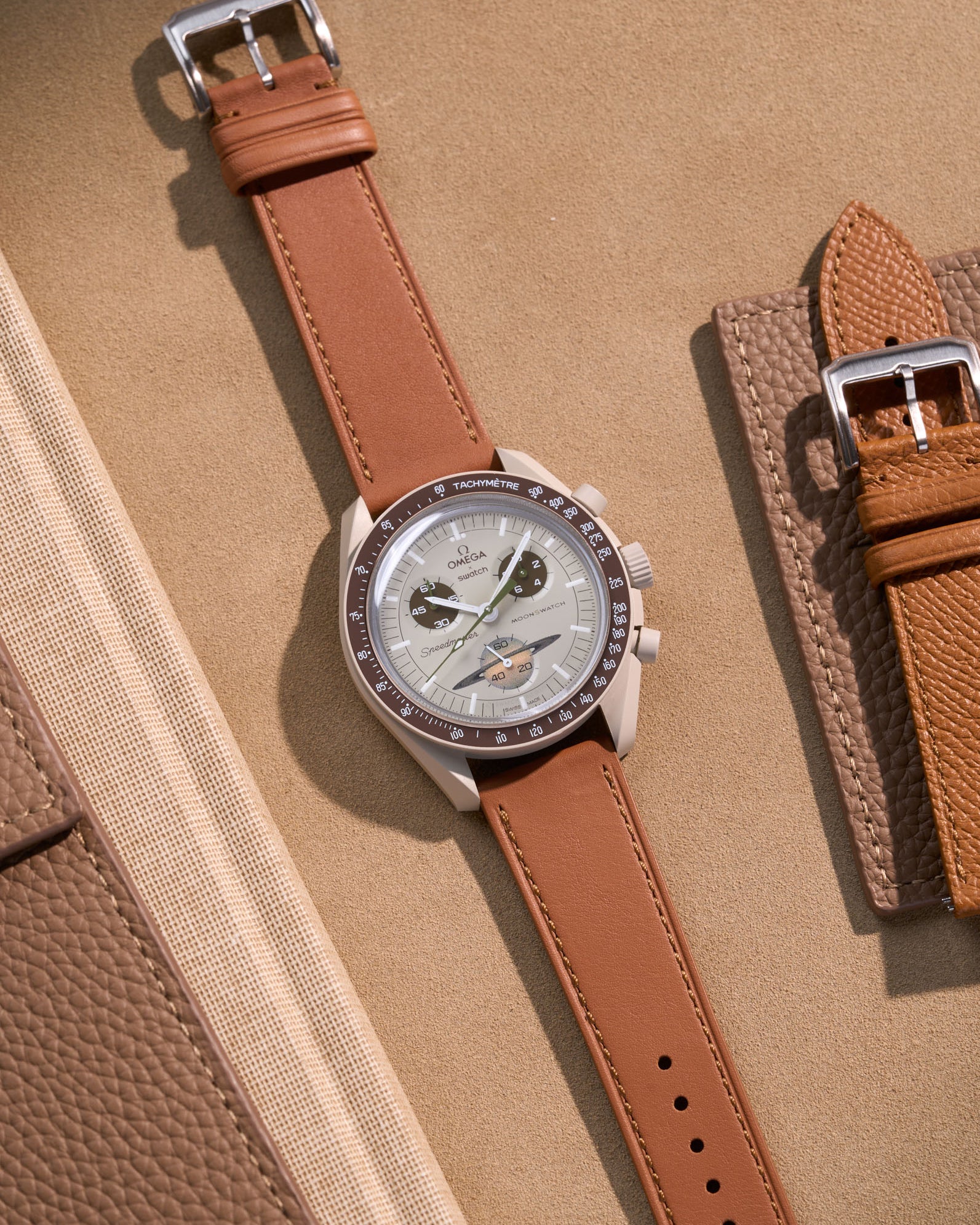 Flat lay of Omega X Swatch Mission to Saturn with Brown cowhide leather strap, styled with neutral and warm brown accessories