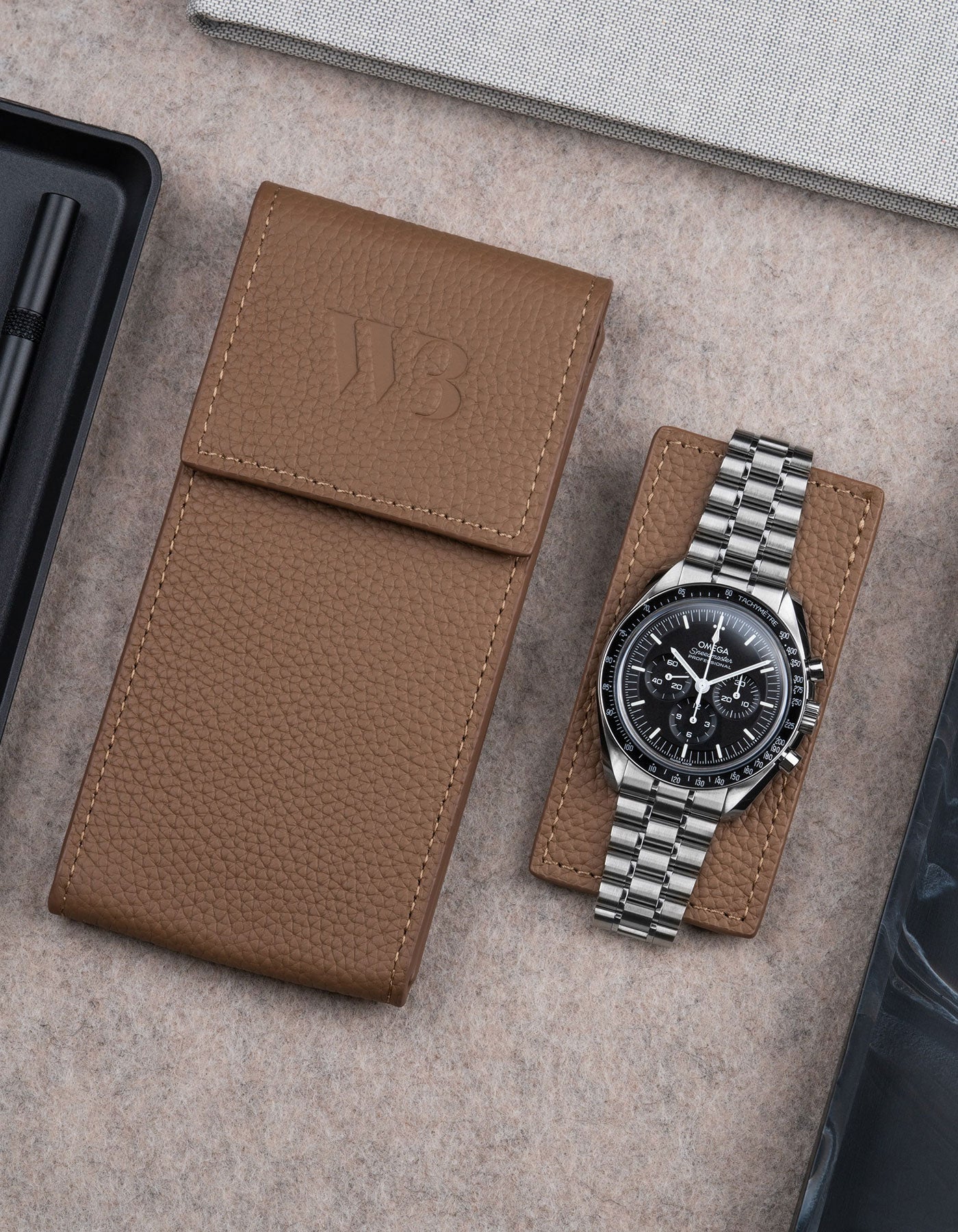 Brown leather watch pouch by Wristbuddys with Omega Speedmaster placed alongside closed case – stylish leather travel pouch for watches