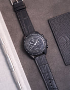 Flat lay of Omega X Swatch MoonSwatch Mission to the Moonphase New Moon with black embossed alligator leather strap
