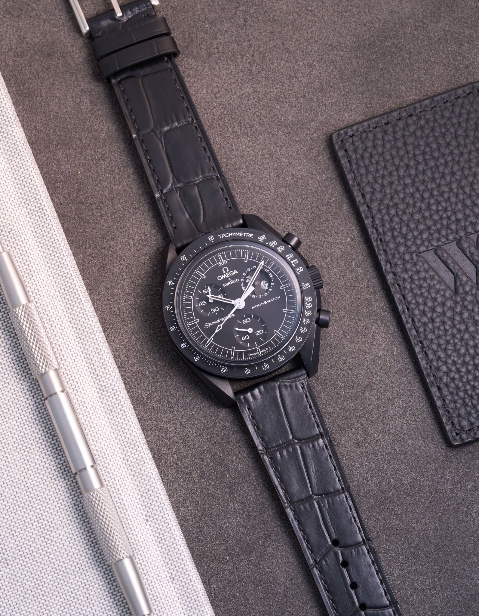 Flat lay of Omega X Swatch MoonSwatch Mission to the Moonphase New Moon with black embossed alligator leather strap