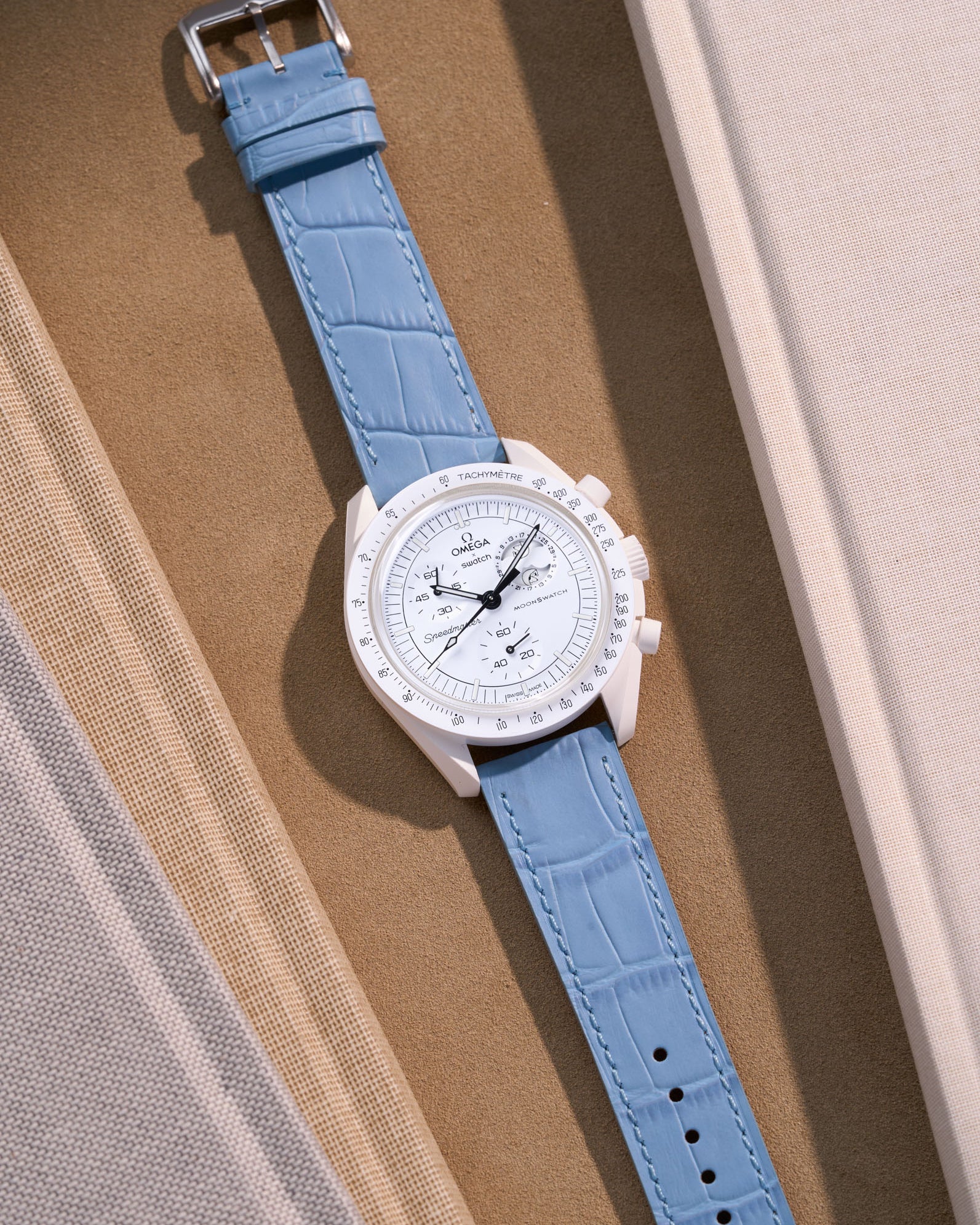 Flat lay of Omega X Swatch MoonSwatch Mission to the Moonphase Full Moon with sky blue embossed alligator leather strap
