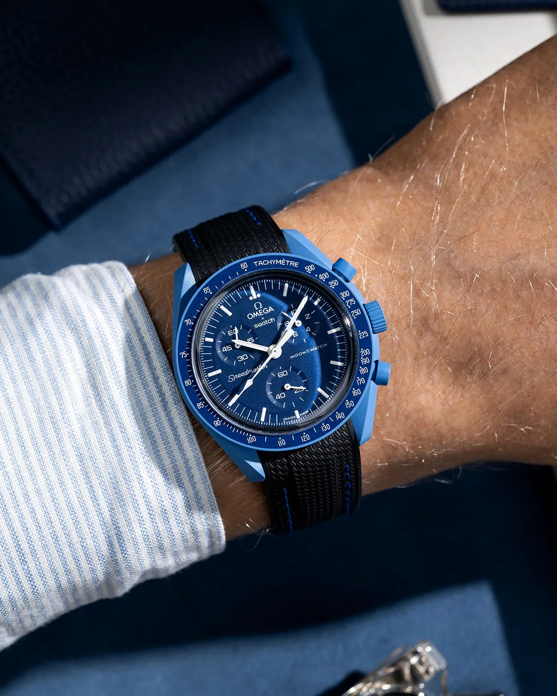 Black rubber strap with blue stitching on Omega MoonSwatch Neptune, shown on wrist with sporty summer aesthetic