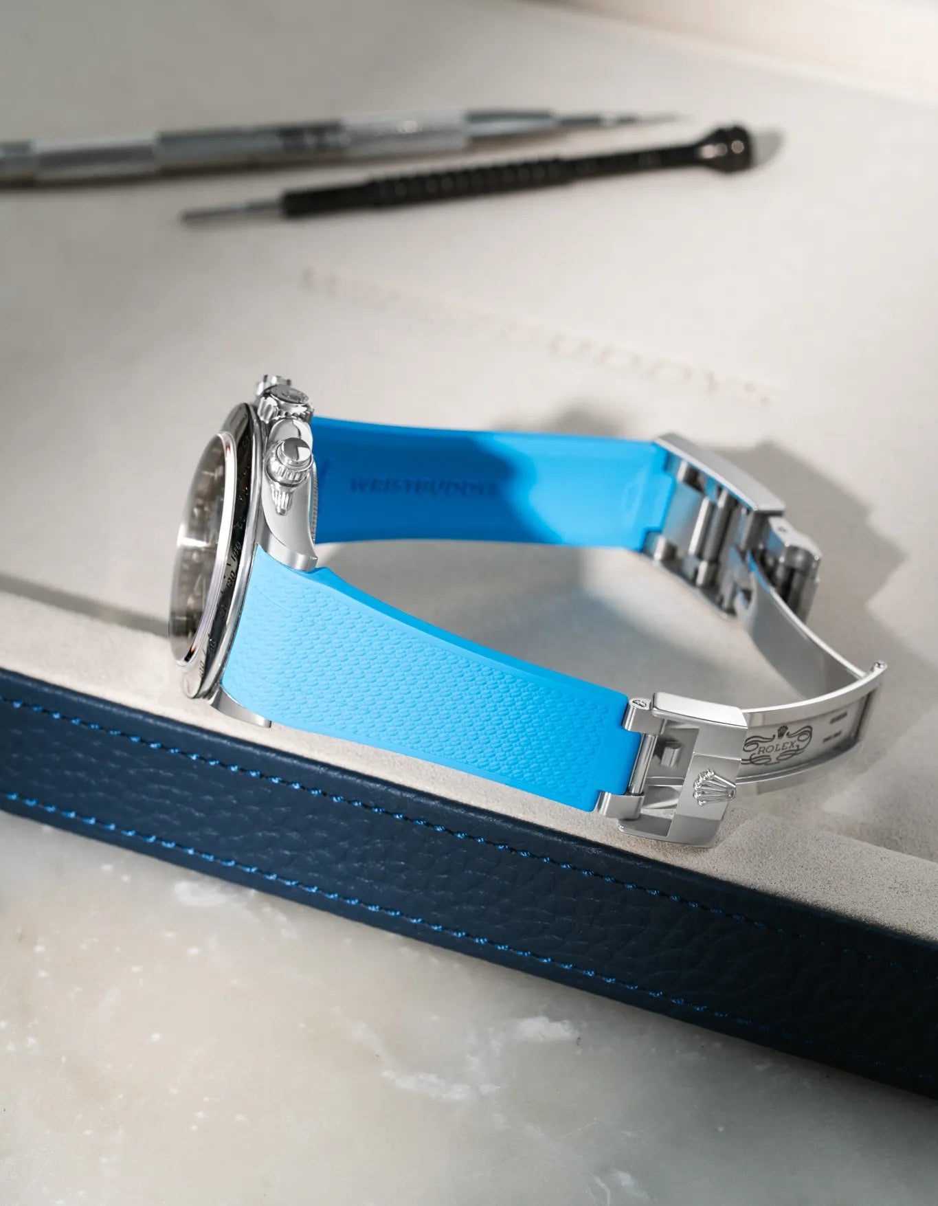 Capri Blue integrated FKM rubber watch strap for Rolex Daytona 116520, Vertech textured finish, fits original clasp on a grey valet tray.