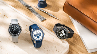 Three Omega Speedmaster Moonwatch chronographs on light grey, navy blue, and black rubber straps, styled with spring bar tool and leather bag — Wristbuddys Speedmaster collection