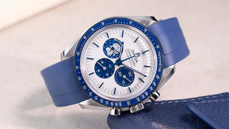 Omega Speedmaster watch with blue FKM rubber strap placed on light surface next to blue leather watch pouch