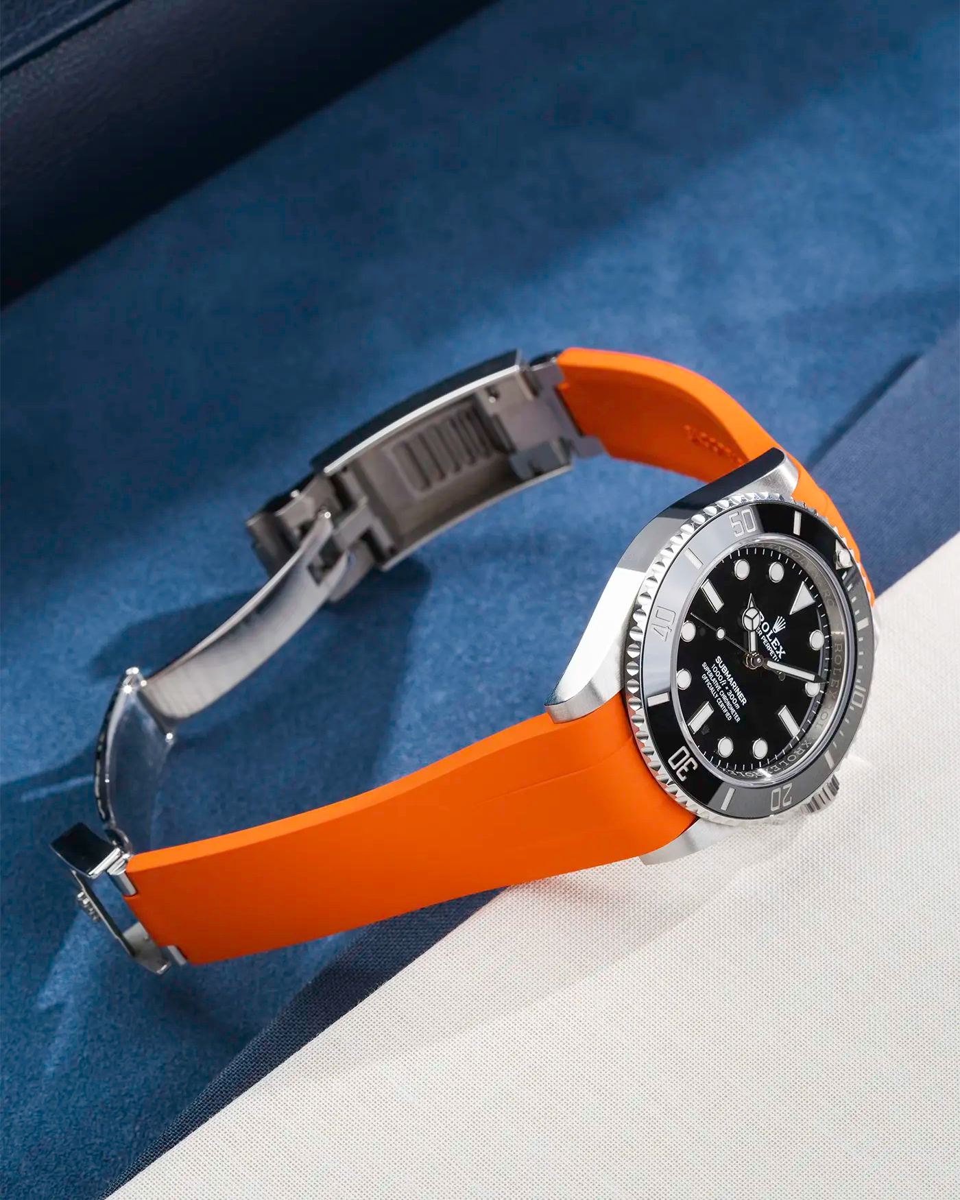 Lifestyle product photo of Rolex Submariner 41 with orange Classic Smooth FKM Rubber Strap mounted on the watch, integrated with original clasp – side angle view showing clasp open