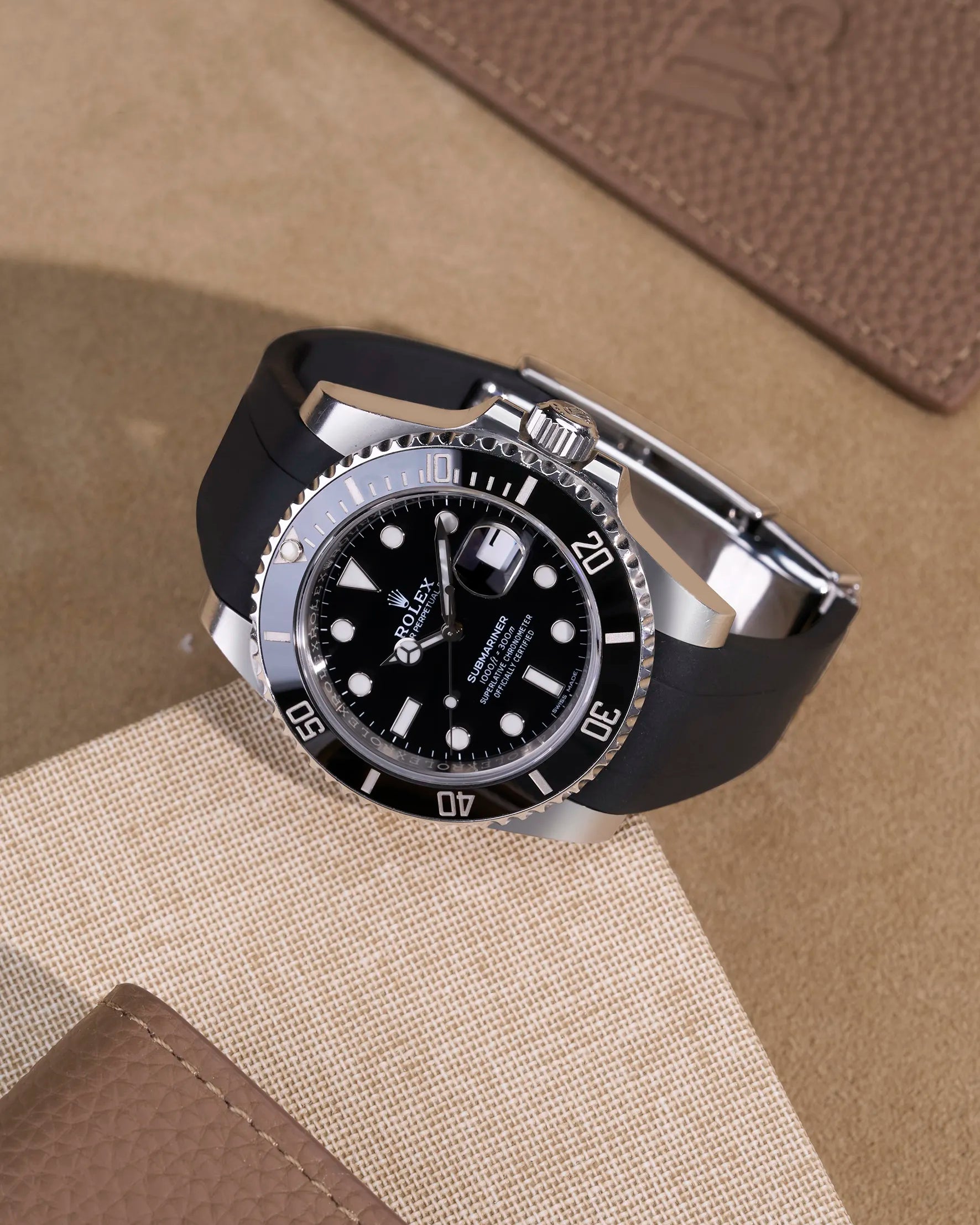 Black FKM rubber strap on Rolex Submariner 116610LN with clasp, flatlay on leather surface