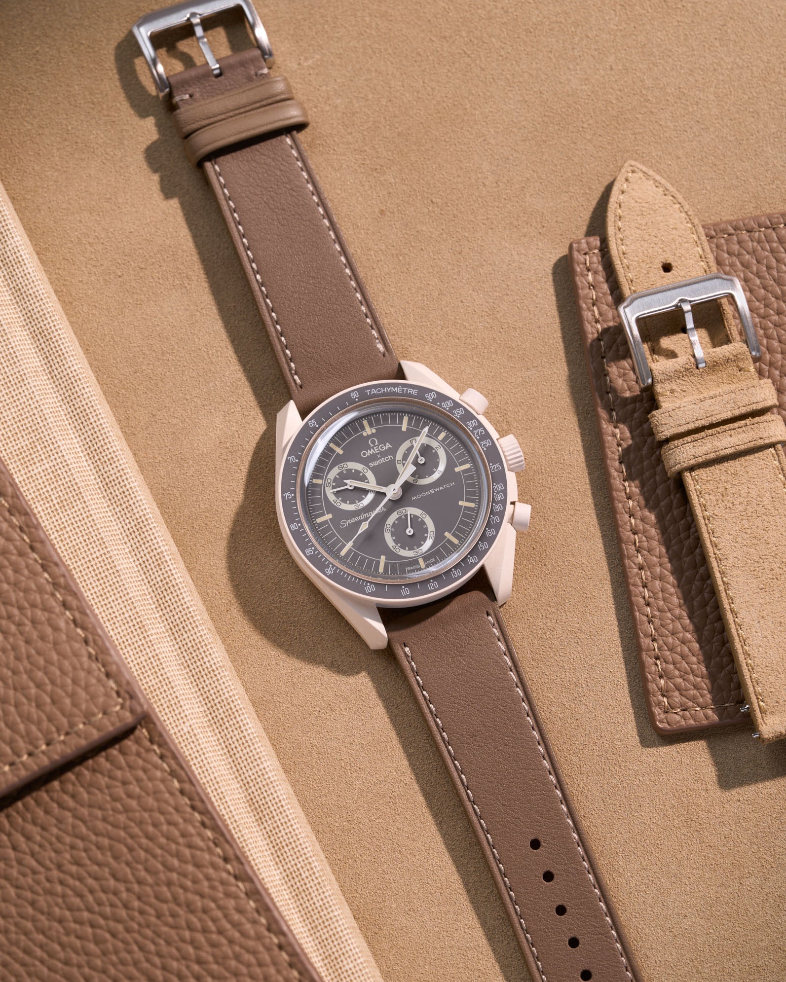 Flat lay of Omega X Swatch Mission on Earth – Desert with Taupe cowhide leather strap, styled with accessories