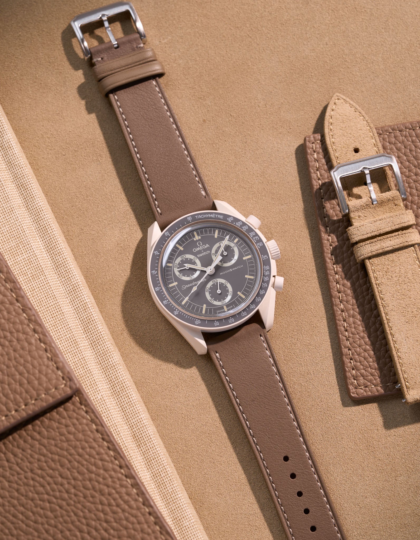 Flat lay of Omega X Swatch Mission on Earth – Desert with Taupe cowhide leather strap, styled with accessories