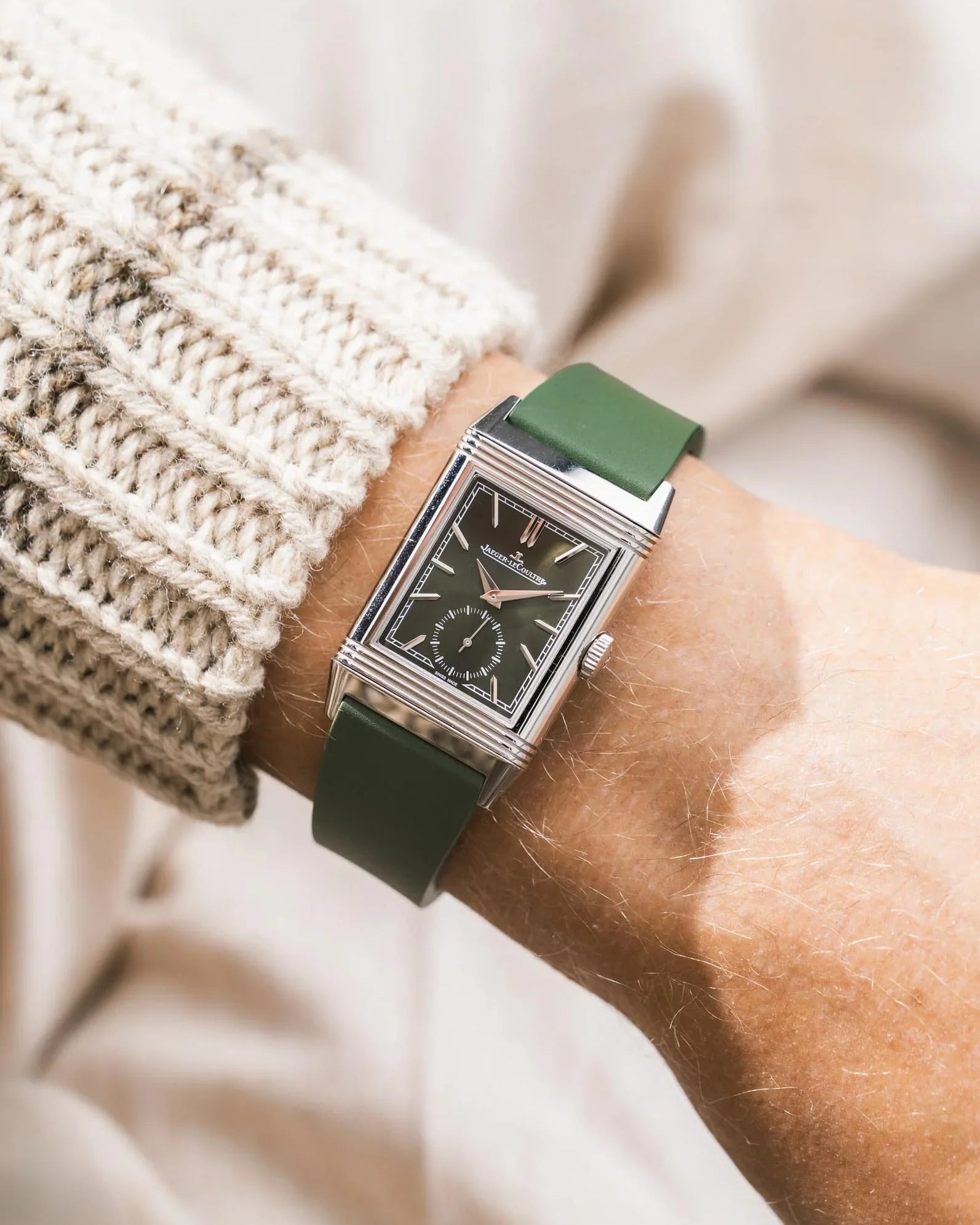 Green CTS rubber watch strap on a JLC Reverso on a person's wrist with a blurred background