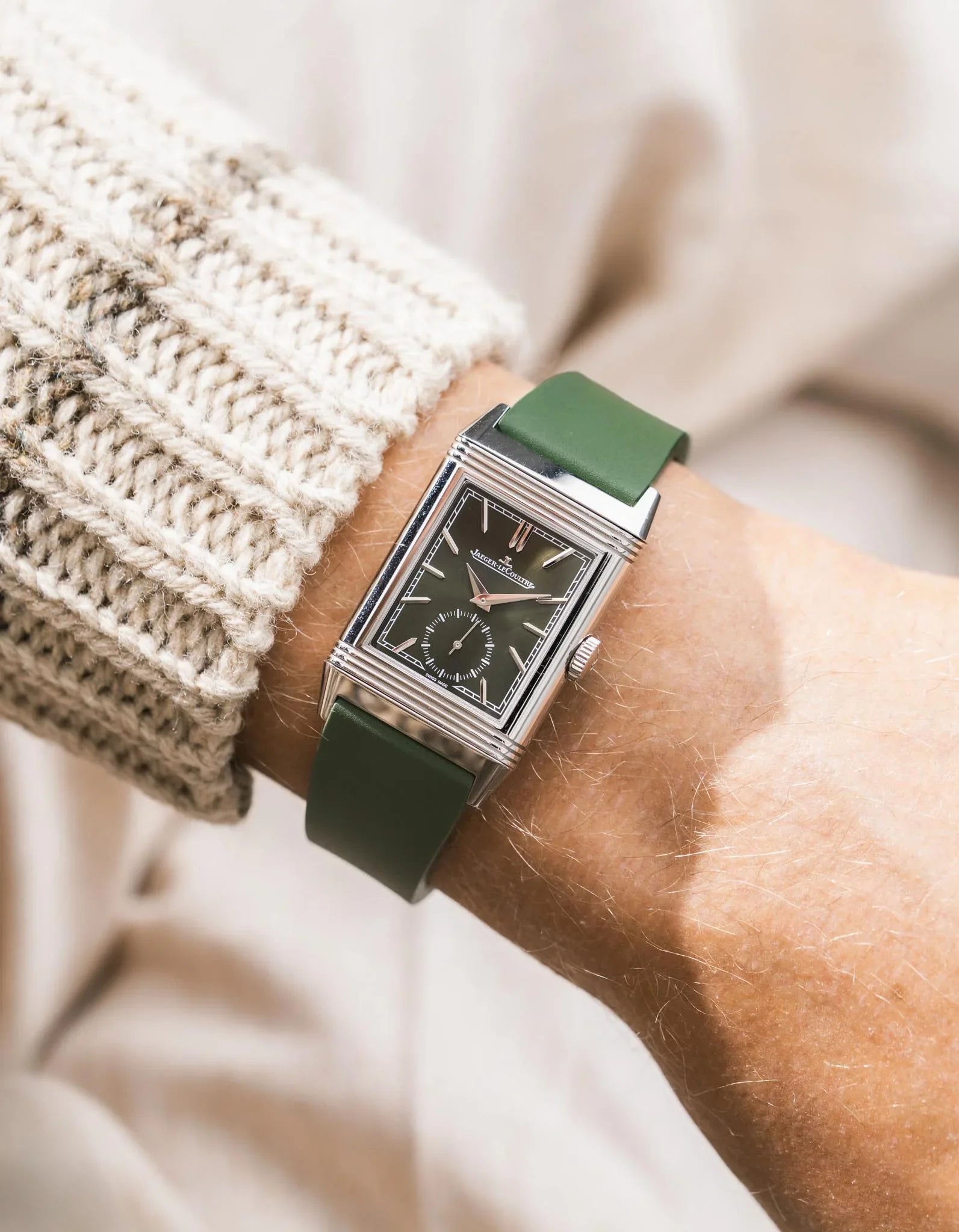 Green CTS rubber watch strap on a JLC Reverso on a person's wrist with a blurred background