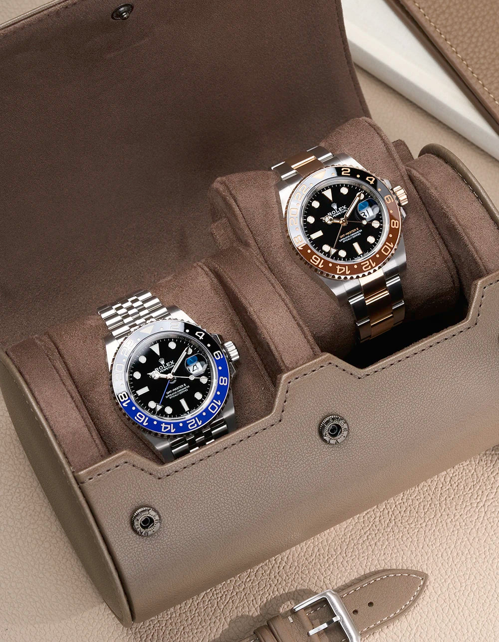 Rolex GMT Batgirl and Rolex GMT Rootbeer in a watch roll on a taupe surface