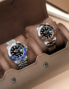 Two watches in a brown watch holder with a neutral background