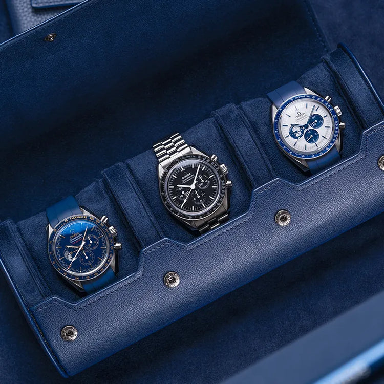 Navy blue 3 slot watch roll with suede interior holding three Omega watches on blue surface