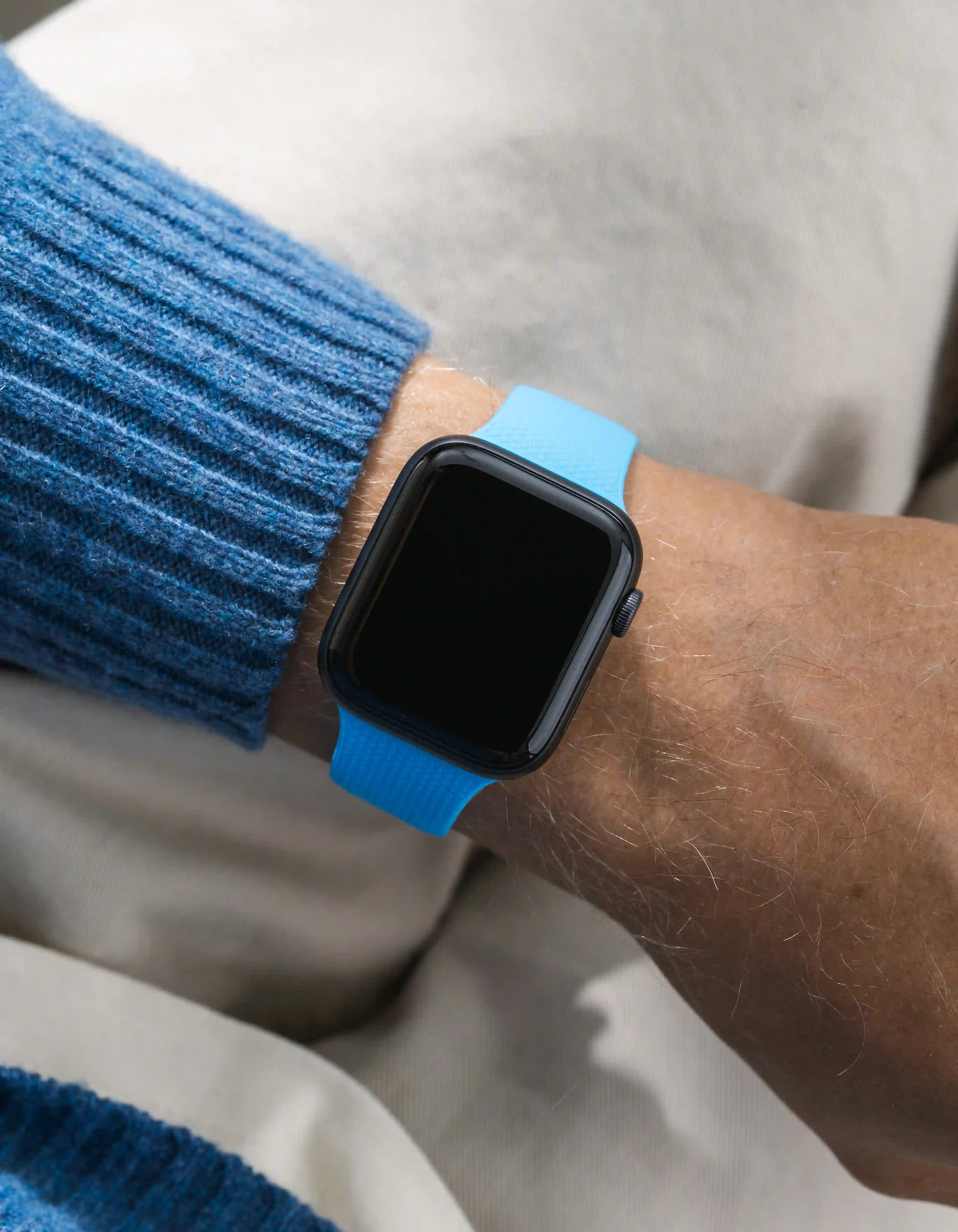 Smartwatch with a blue band on a wrist, wearing a blue sweater.