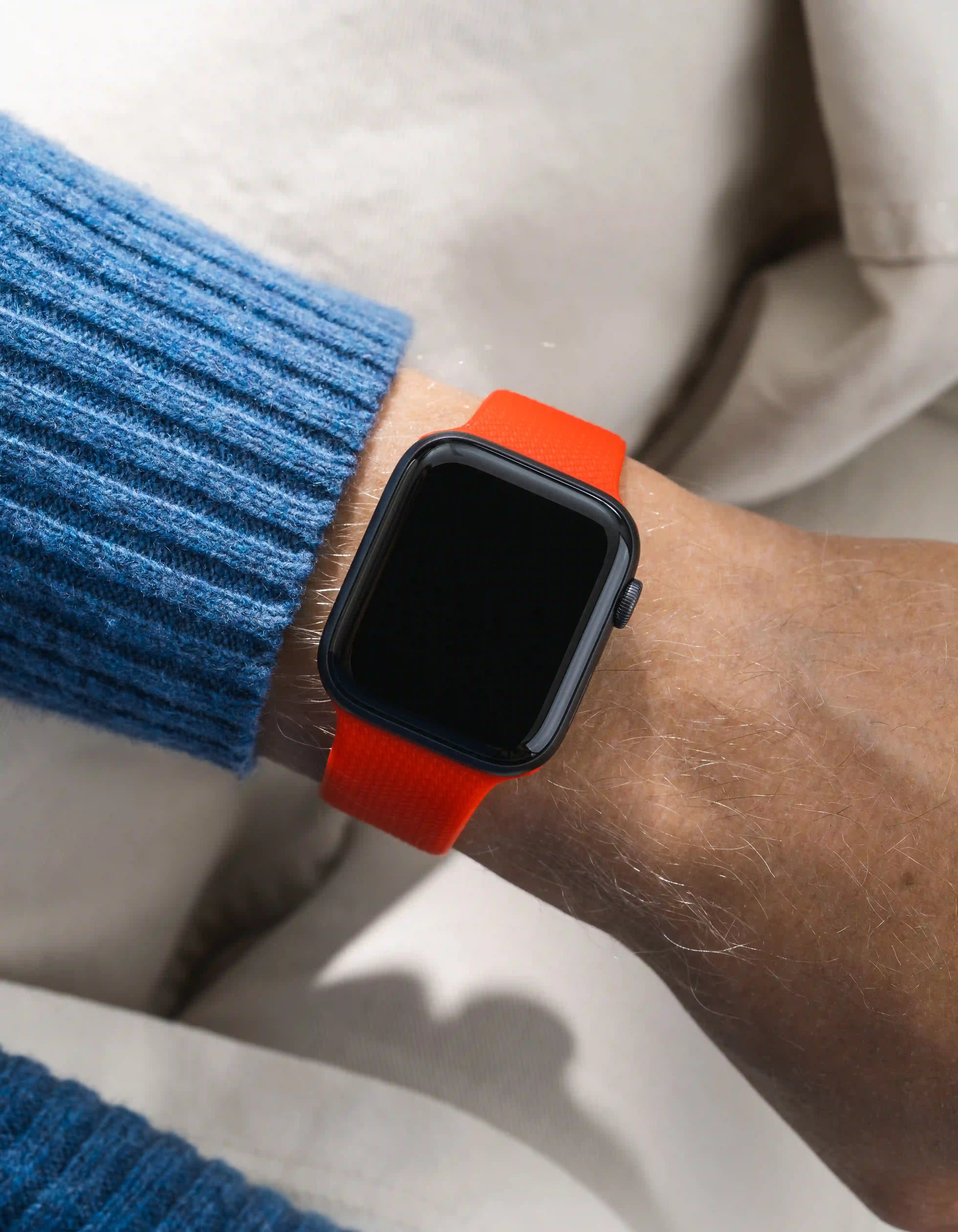 Smartwatch with an orange red on a wrist wearing a blue sweater.