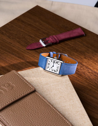 Baltic Blue suede strap on Cartier Tank watch placed on beige leather | styled scene with burgundy strap in background