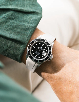 Beige FKM rubber strap integrated for original clasp on Rolex Submariner 16610LN full steel, black ceramic bezel, black dial, straight front-facing wrist shot, smooth strap texture, dark green linen shirt sleeve, cream trousers background