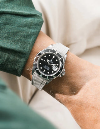 Beige Vertech FKM rubber strap integrated for original clasp on Rolex Submariner 16610LN full steel, black ceramic bezel, black dial, straight front-facing wrist shot, Vertech crosshatch texture clearly visible on beige strap, dark green linen shirt sleeve, cream trousers background