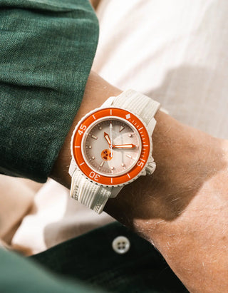Beige Vertech rubber strap for Blancpain x Swatch Scuba Fifty Fathoms Arctic Ocean – worn on wrist with dark green linen jacket, grey dial and orange bezel with white case, side angle view