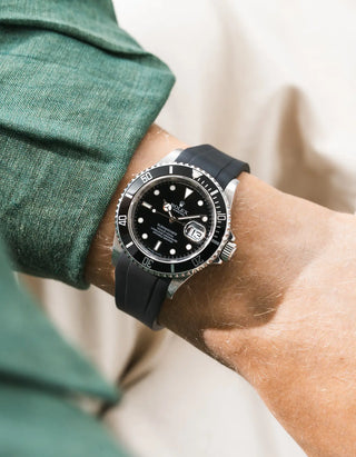 Black FKM rubber strap integrated for original clasp on Rolex Submariner 16610LN full steel, black ceramic bezel, black dial, angled wrist shot from left side, smooth black strap, green linen shirt cuff, beige background
