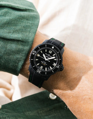 Black Vertech rubber strap with green stitching for Blancpain x Swatch Scuba Fifty Fathoms The Ocean of Storms – worn on wrist with dark green linen shirt, black dial and black bezel with black case, side angle view
