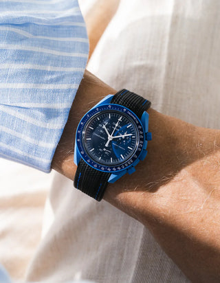 Black rubber strap with white stitching fitted to an OMEGA x Swatch MoonSwatch Mission to Neptune watch, worn on the wrist in a lifestyle shot with clothing visible