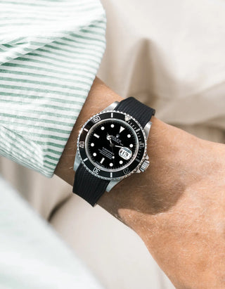 Black Vertech FKM rubber strap integrated for original clasp on Rolex Submariner 16610LN full steel, black ceramic bezel, black dial, angled wrist shot from left side, Vertech crosshatch texture clearly visible on strap, green and white striped shirt cuff, white background