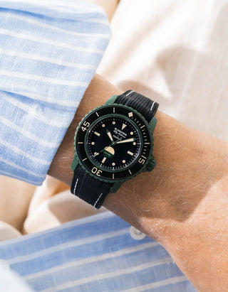 Black Vertech rubber strap with white stitching for Blancpain x Swatch Scuba Fifty Fathoms Green Abyss – worn on wrist with light blue striped shirt, black dial and black bezel with green case, side angle view