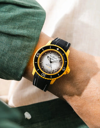 Black Vertech rubber strap with white stitching for Blancpain x Swatch Scuba Fifty Fathoms Pacific Ocean – worn on wrist with dark green linen jacket, white dial and black bezel with yellow case, front angle view