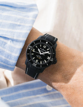 Black Vertech rubber strap with white stitching for Blancpain x Swatch Scuba Fifty Fathoms The Ocean of Storms – worn on wrist with light blue striped shirt, black dial and black bezel with black case, front angle view