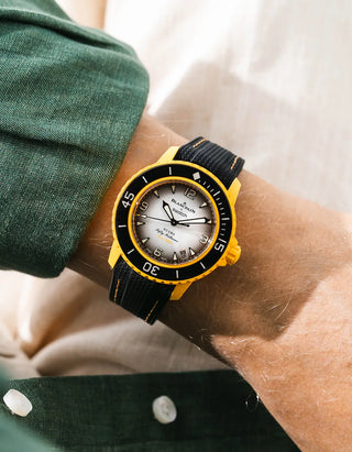 Black Vertech rubber strap with yellow stitching for Blancpain x Swatch Scuba Fifty Fathoms Pacific Ocean – worn on wrist with dark green linen jacket, white dial and black bezel with yellow case, side angle view
