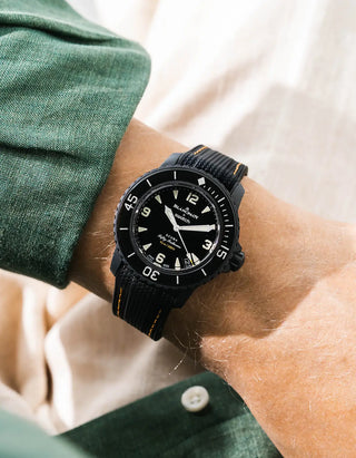 Black Vertech rubber strap with yellow stitching for Blancpain x Swatch Scuba Fifty Fathoms The Ocean of Storms – worn on wrist with dark green linen shirt, black dial and black bezel with black case, side angle view