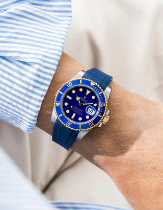 Blue FKM rubber strap integrated for original clasp on Rolex Submariner 116610LB Bluesy two-tone steel and yellow gold, blue ceramic bezel, blue dial, straight front-facing wrist shot, smooth strap texture, blue striped shirt cuff, white background