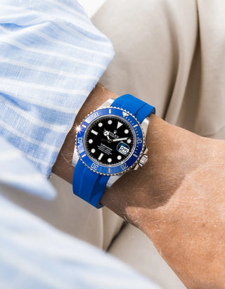 Blue FKM rubber strap integrated for original clasp on Rolex Submariner 126619LB "Cookie Monster" 18k white gold, blue ceramic bezel, black dial, straight front-facing wrist shot, smooth royal blue strap matching bezel color, light blue striped linen shirt sleeve, cream background
