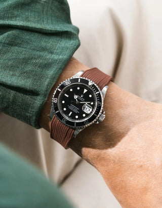 Brown Vertech FKM rubber strap integrated for original clasp on Rolex Submariner 16610LN full steel, black ceramic bezel, black dial, angled top-down wrist shot, Vertech crosshatch texture clearly visible on brown strap, dark green linen shirt sleeve, beige background