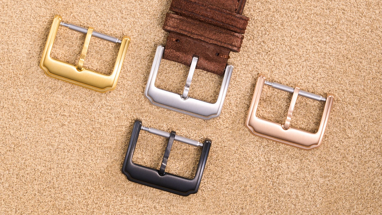 Leather watch buckles in gold, silver, black, and rose gold displayed on beige suede surface.