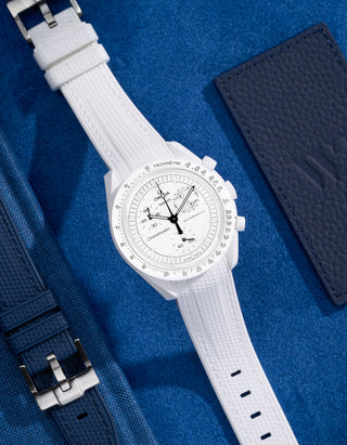 Flat lay of MoonSwatch Mission to the Moonphase with white vertech strap and accessories in background
