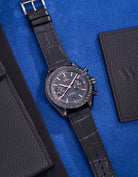 Omega Dark Side of the Moon watch paired with black alligator leather strap on a vibrant blue surface