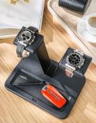 Two luxury watches displayed on the Wristbuddys Double Watch Stand on a wooden desk, next to an espresso and a watch book