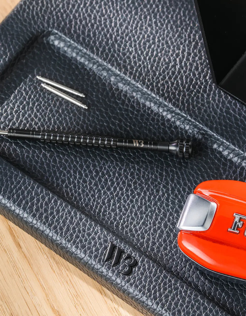 Detail of the watch stand tray holding spring bars and a Wristbuddys watch tool, with the embossed WB logo visible on the leather base