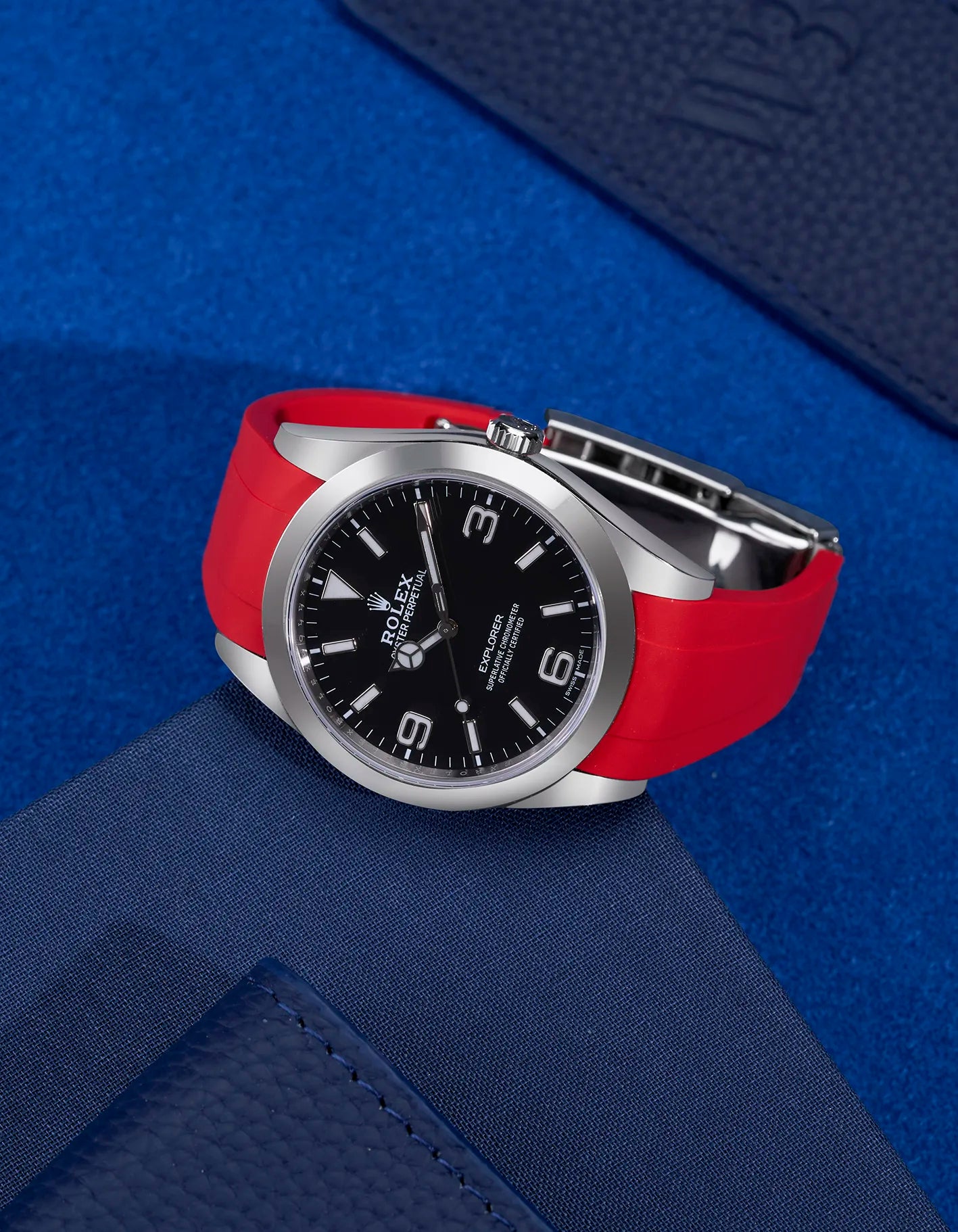 Rolex Explorer 214270 paired with red rubber strap and original clasp – flat lay on blue background