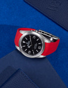 Rolex Explorer 214270 paired with red rubber strap and original clasp – flat lay on blue background