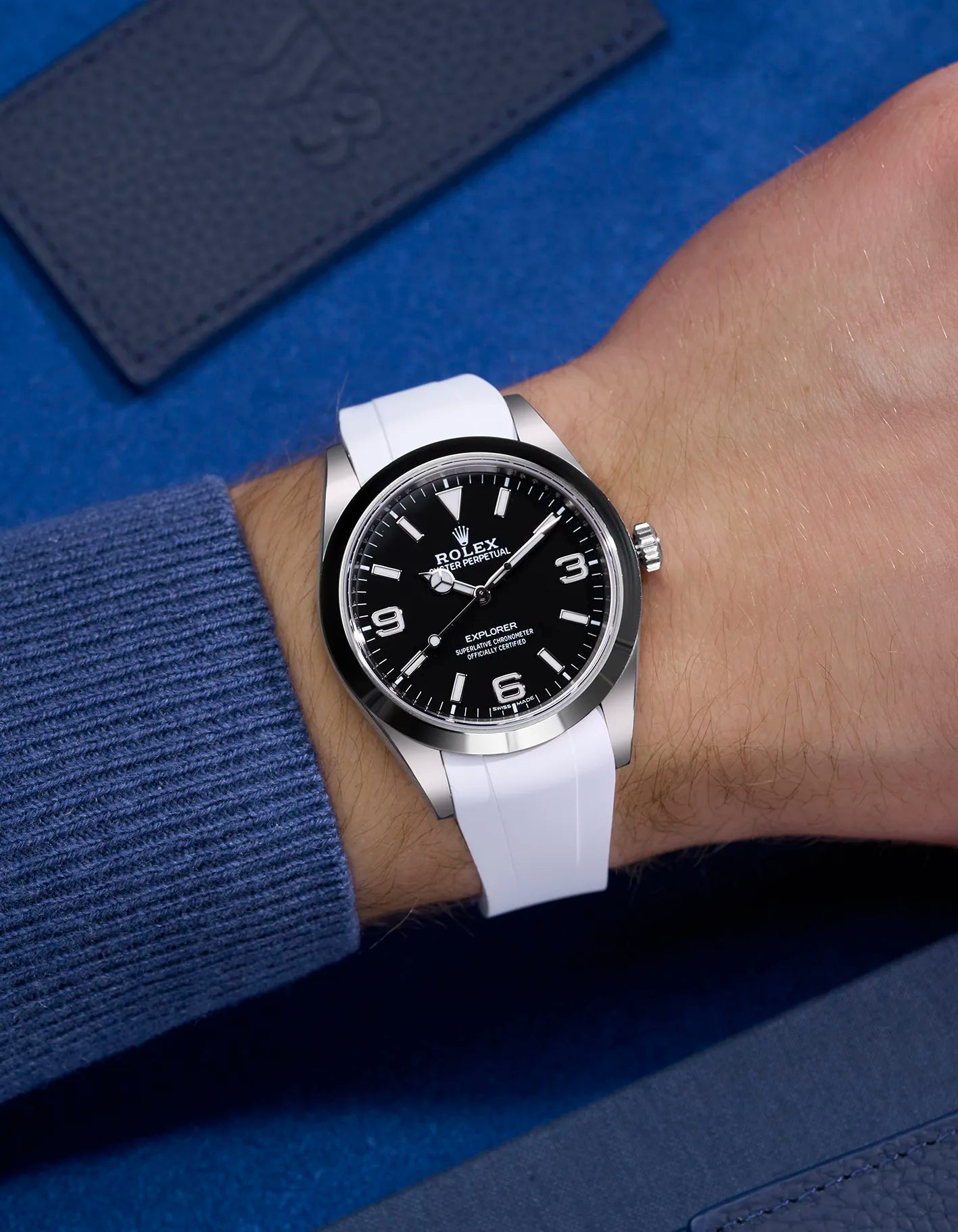 White rubber strap integrated with original clasp on Rolex Explorer 214270 – wrist shot against blue background