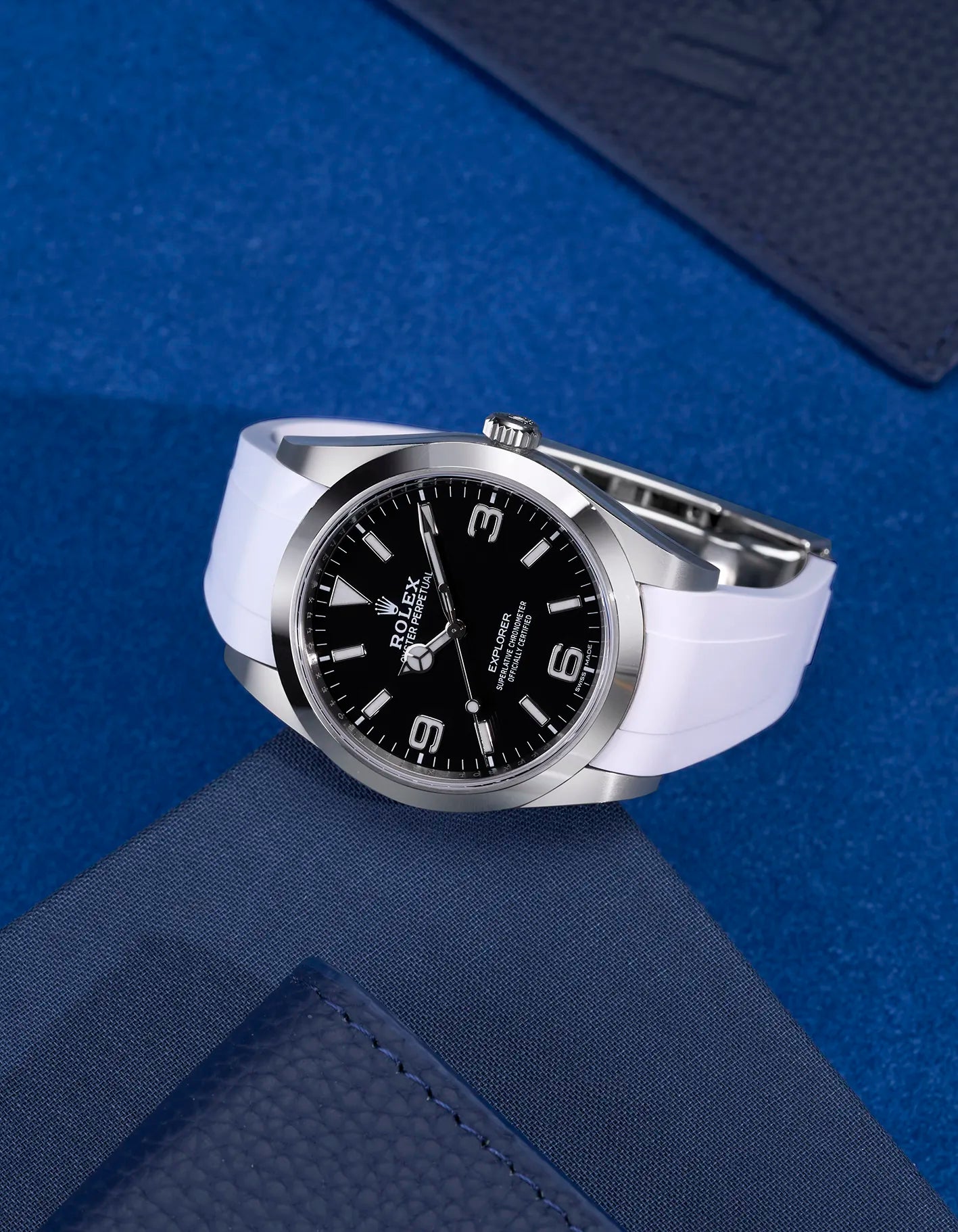 Rolex Explorer 214270 fitted with white rubber strap and original clasp – flat lay on dark blue surface