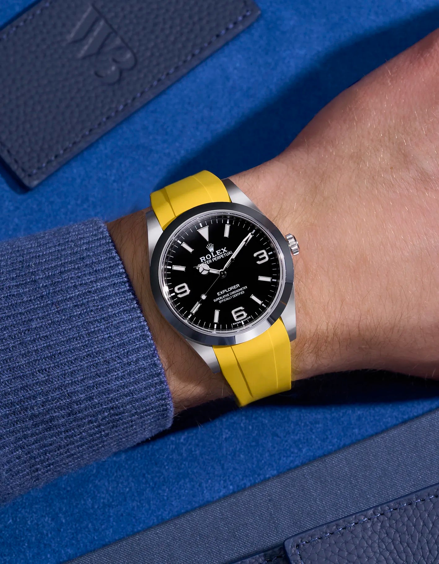 Rolex Explorer 214270 on wrist with integrated yellow rubber strap and original clasp – blue contrast backdrop